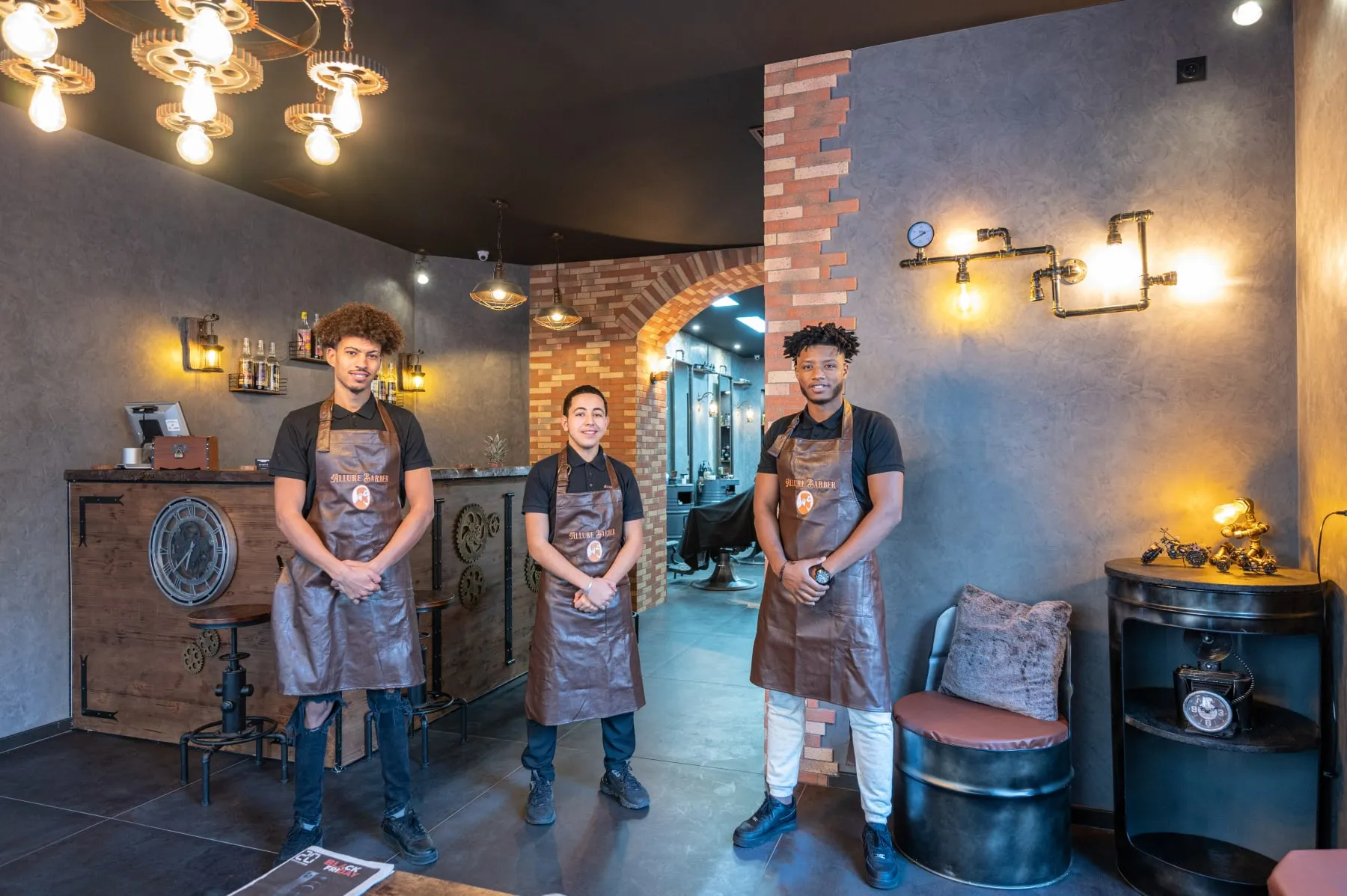 Trois barbiers d'Allure Barber devant l'arche de briques du salon.